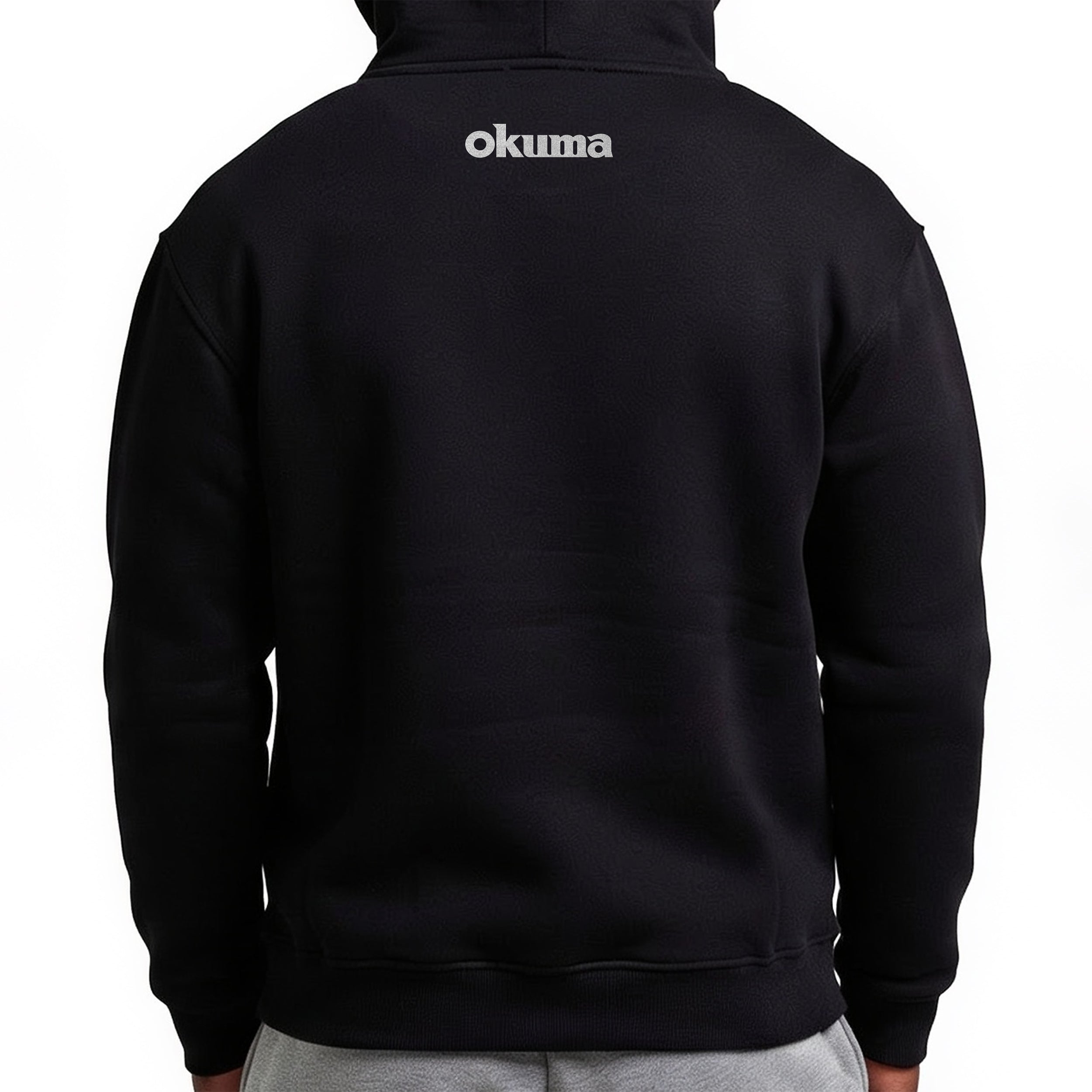 A person viewed from the back wearing a black pullover hoodie with the brand name 'okuma' printed in white across the upper back, paired with light gray sweatpants against a plain white background.