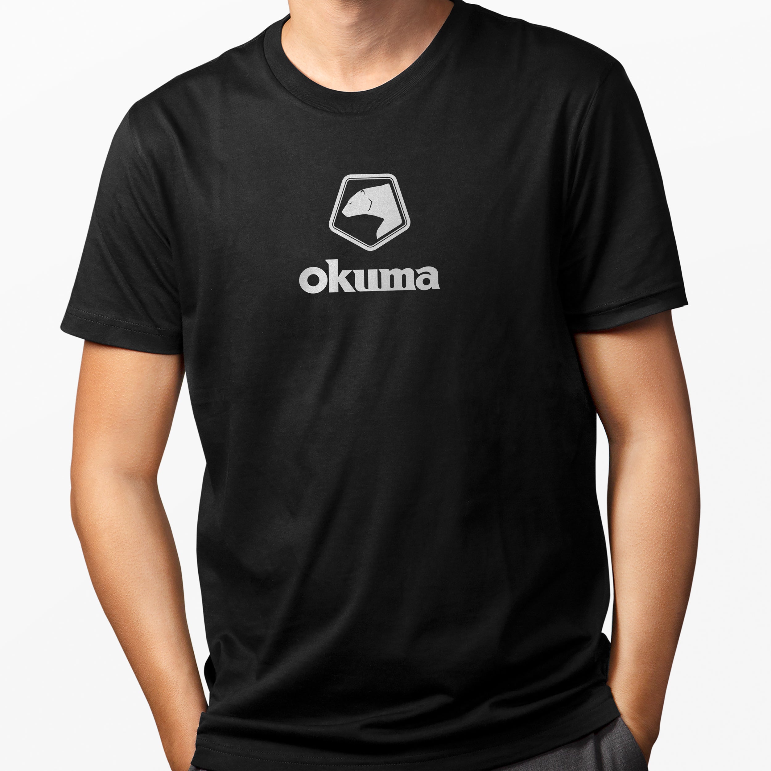 A person wearing a black short-sleeve crewneck t-shirt with a white printed Okuma logo on the chest, shown against a light gray background.