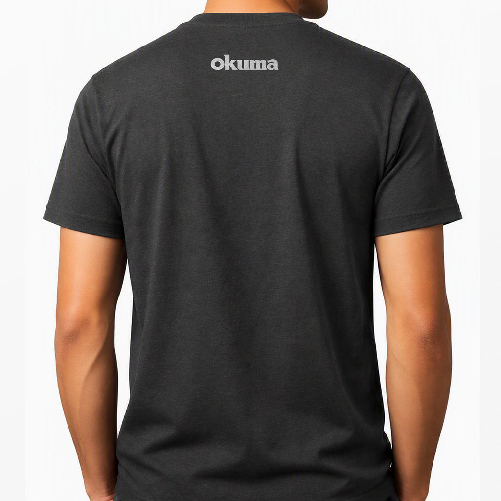 A man wearing a dark charcoal gray t-shirt, viewed from the back. The shirt features the brand name 'okuma' printed in white lowercase letters across the upper back.